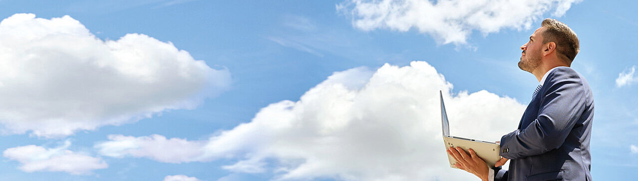 Un homme, ordinateur portable à la main, regarde les nuages en l'air.